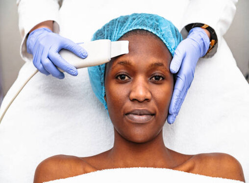 Doctor cosmetologist makes ultrasound cleaning procedure of facial skin of african woman in beauty salon. Close up woman face