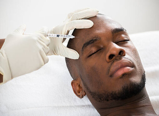 Close-up Of Person Hand Injecting Syringe On Young African Man Face